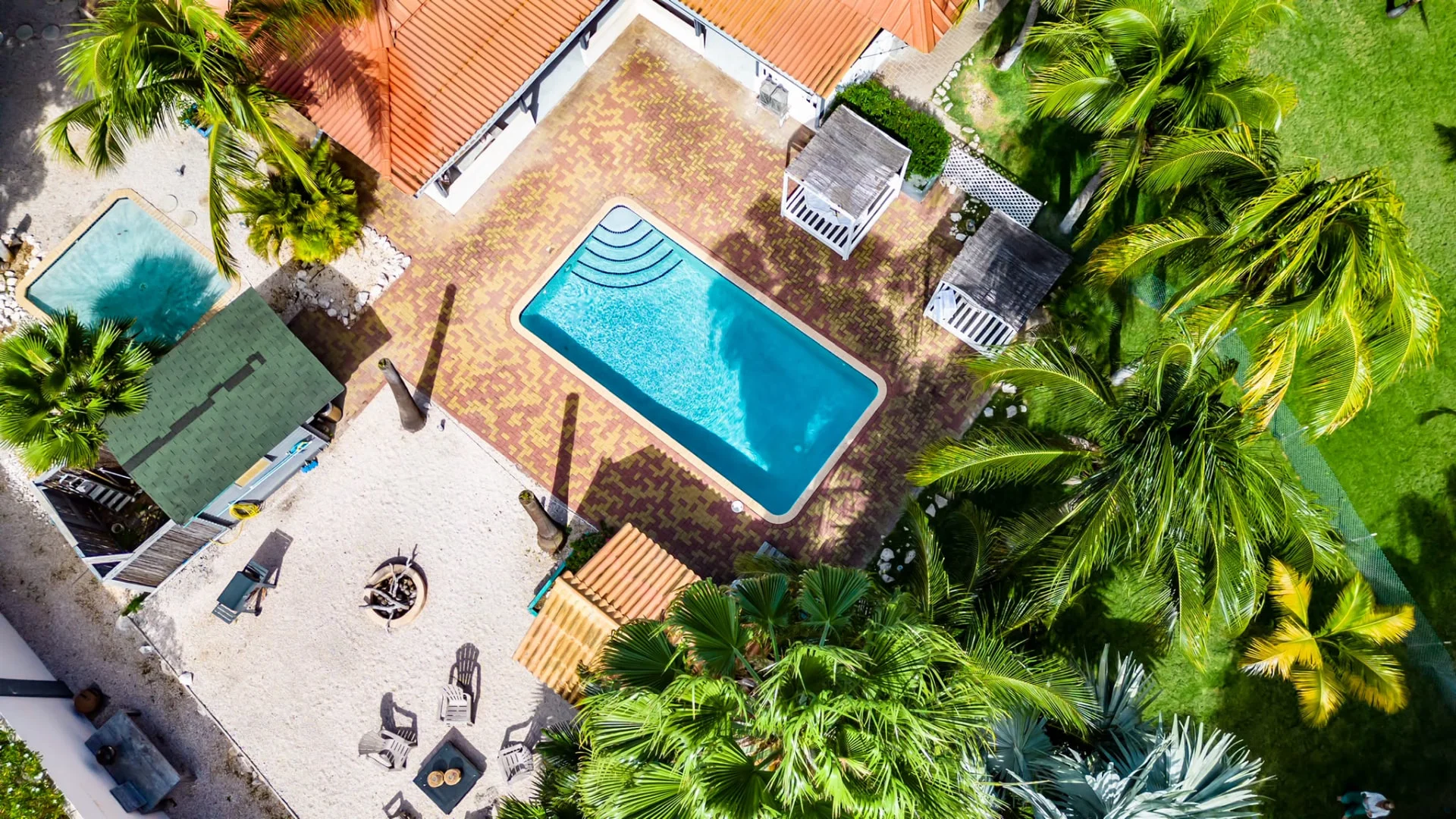 Dronefoto van het zwembad, daybeds en de zithoek in de tropische tuin